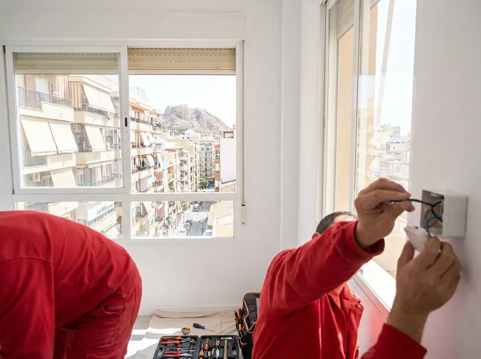 Dos operarios instalando el pulsador de una persiana motorizada junto a una ventana